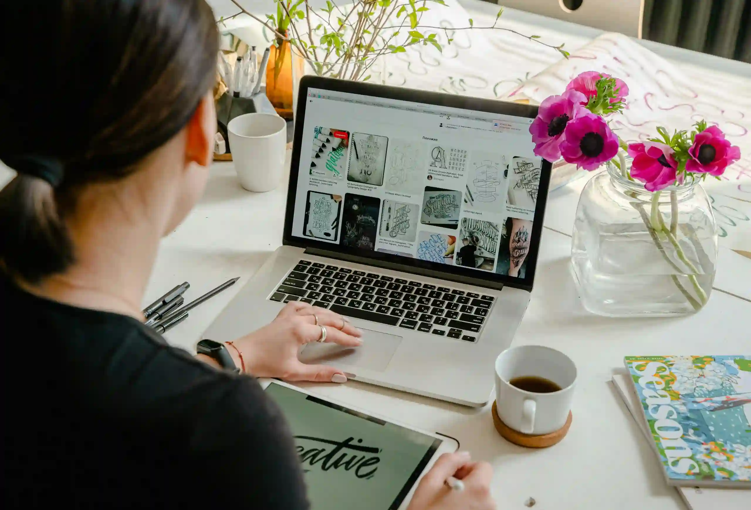 Woman in a creative workspace using a laptop and tablet for typing SEO optimized web content. Artistic and tech-driven environment.